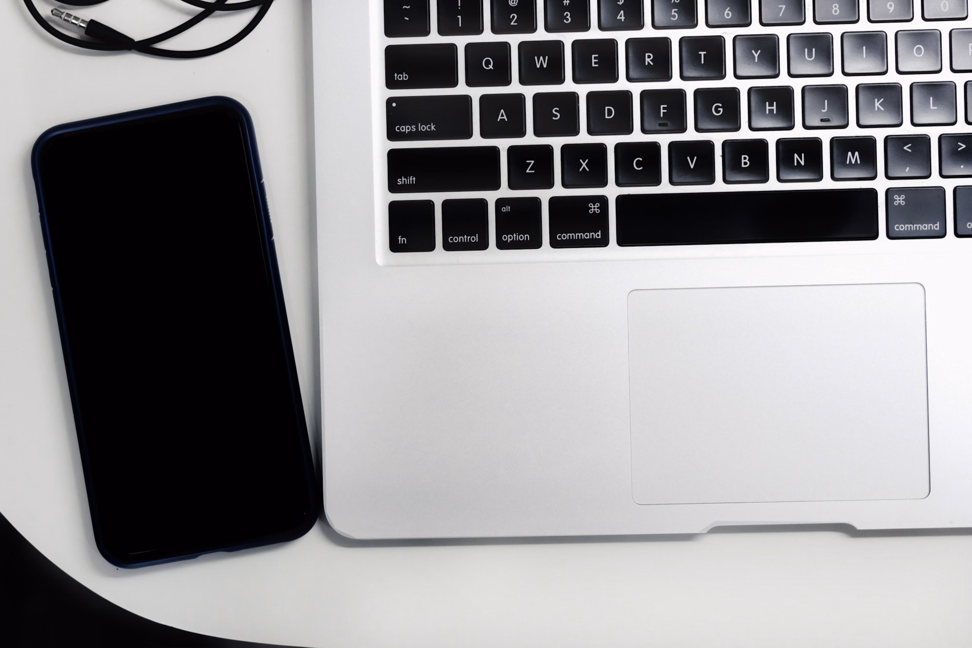 MacBook, Smartphone und Kopfhörer auf einem hellen Schreibtisch – aktuelle Technik als Mitarbeiter-Benefit.