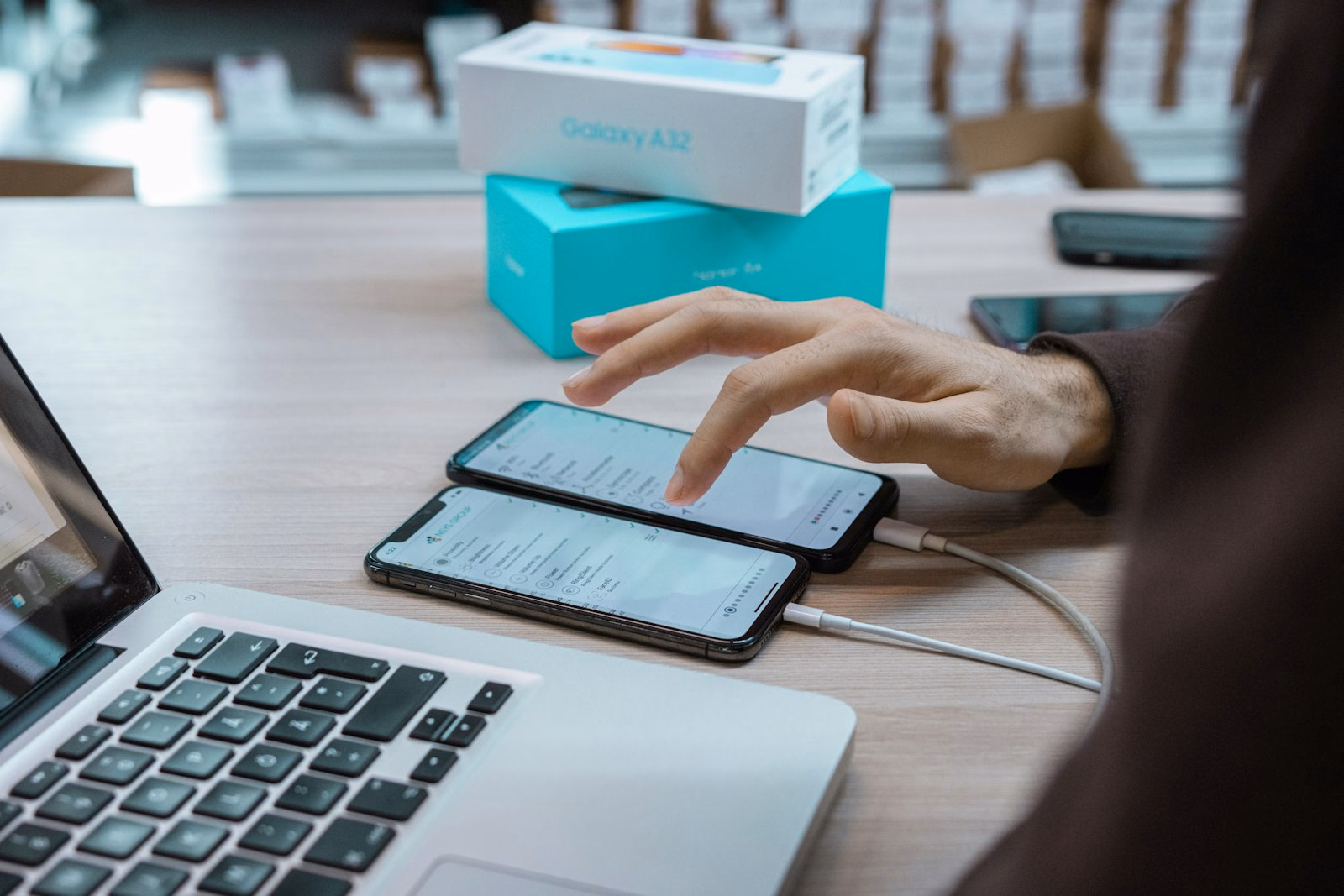 Hand bedient ein Smartphone mit App-Übersicht neben einem aufgeklappten Laptop auf dem Schreibtisch.