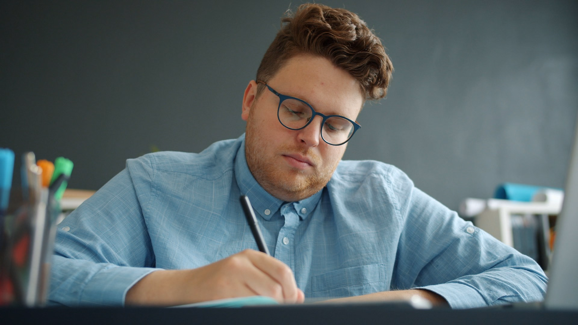 Mann mit Brille sitzt am Schreibtisch und macht sich Notizen.