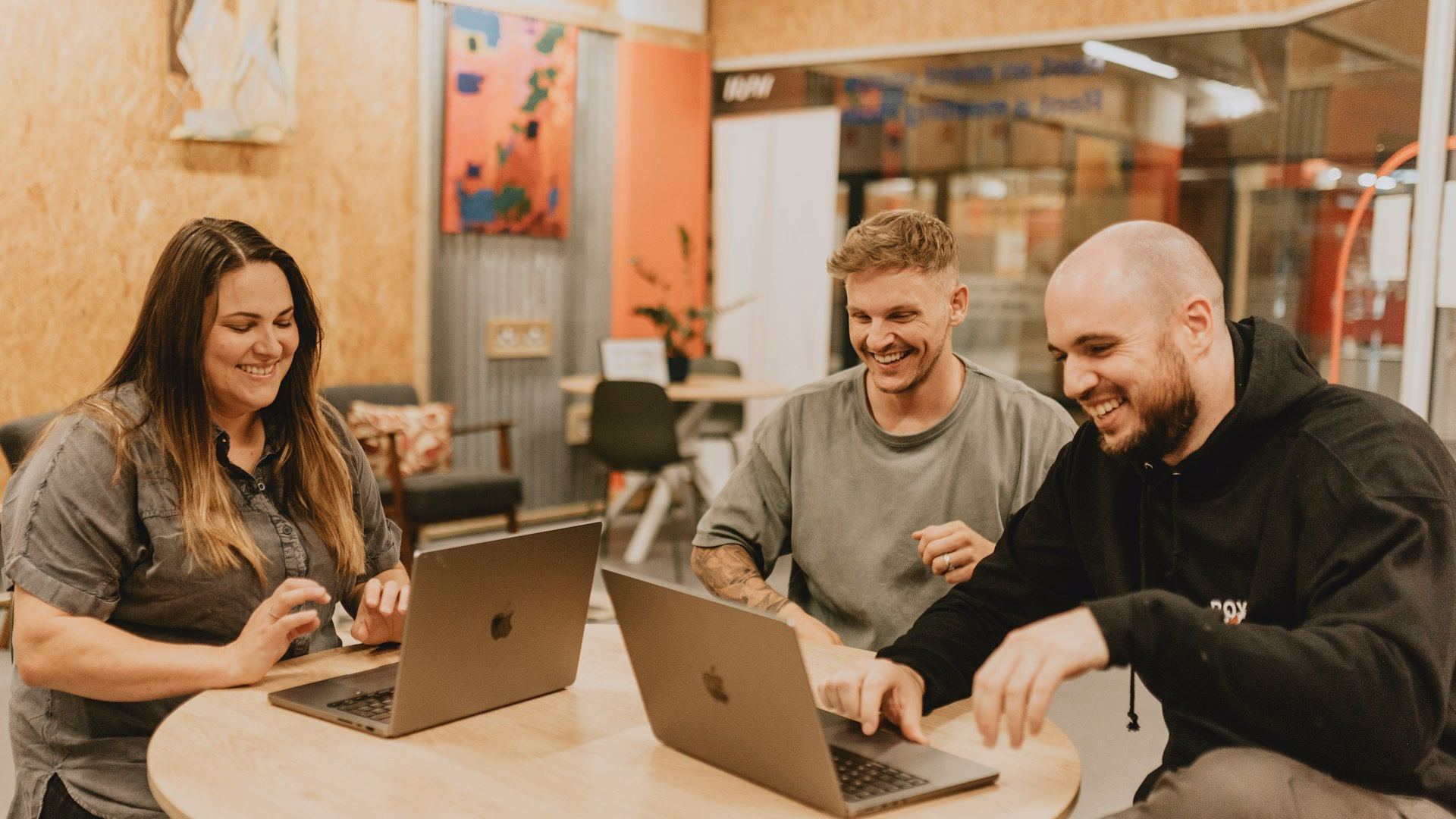 Drei Kolleginnen und Kollegen eines kleinen Teams lachen gemeinsam an zwei Notebooks – Technik-Benefit im Kleinbetrieb.