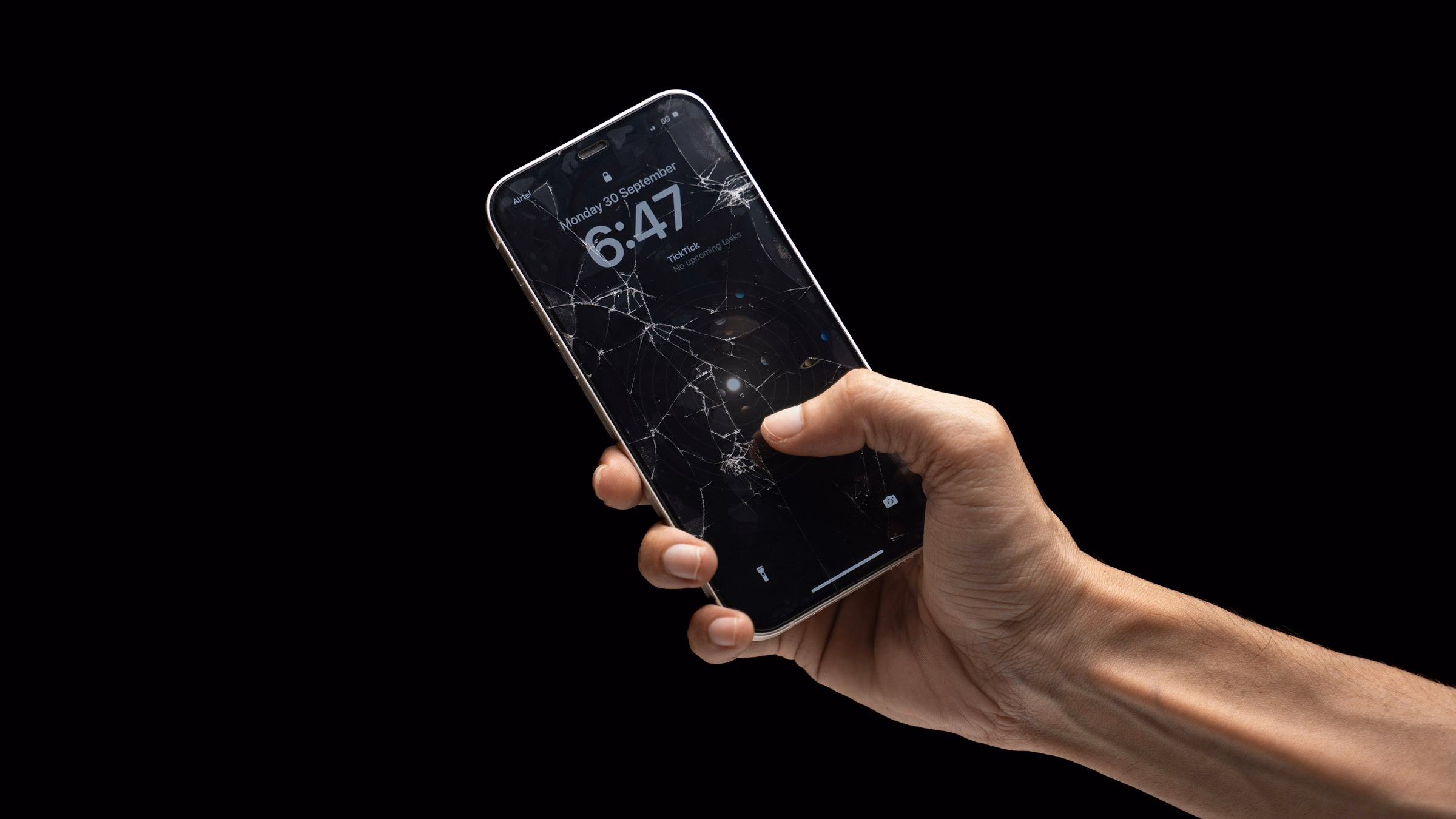 Eine Hand hält ein Smartphone mit gesplittertem Display vor schwarzem Hintergrund – ein typischer Fall für die Versicherung, nicht für die Garantie.