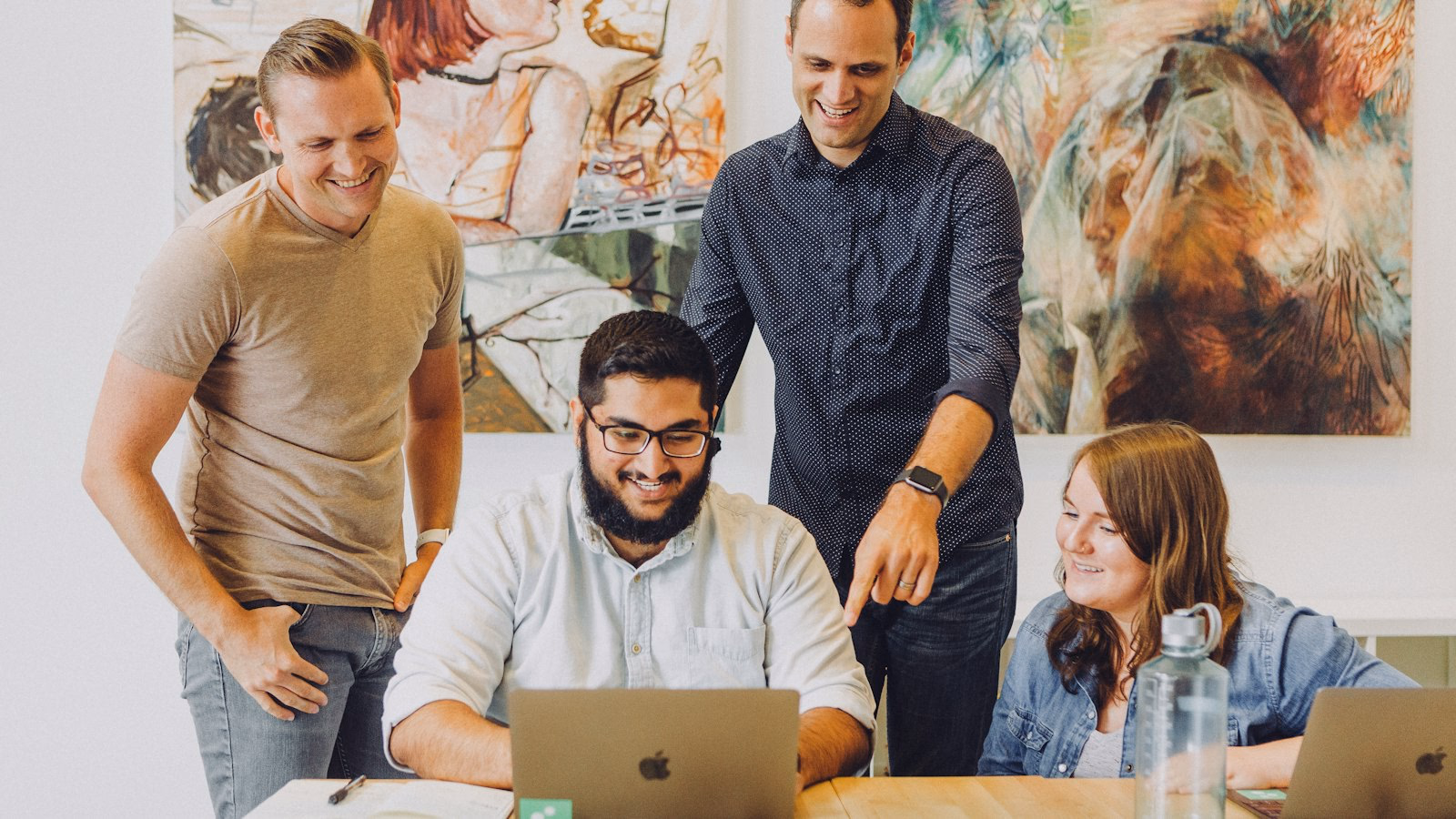 Vier Kolleginnen und Kollegen schauen gemeinsam lächelnd auf einen Laptop – ein Benefit, über das im Team gesprochen wird.