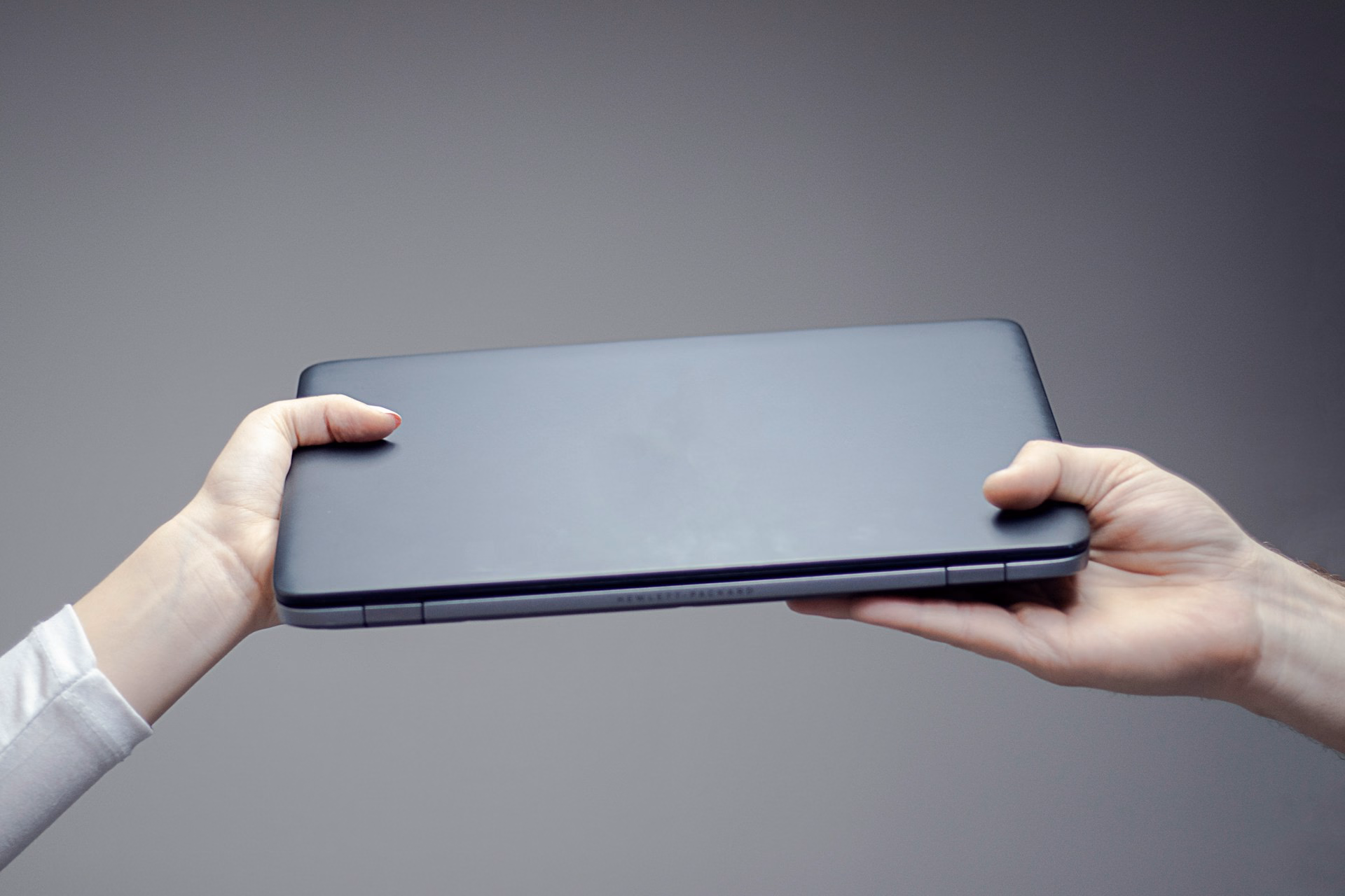 Zugeklapptes Notebook wird von einer Hand an eine andere übergeben.